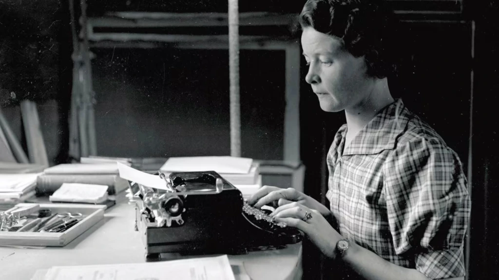Svartvitt fotografi av Sally Salminen som sitter och skriver på en skrivmaskin.