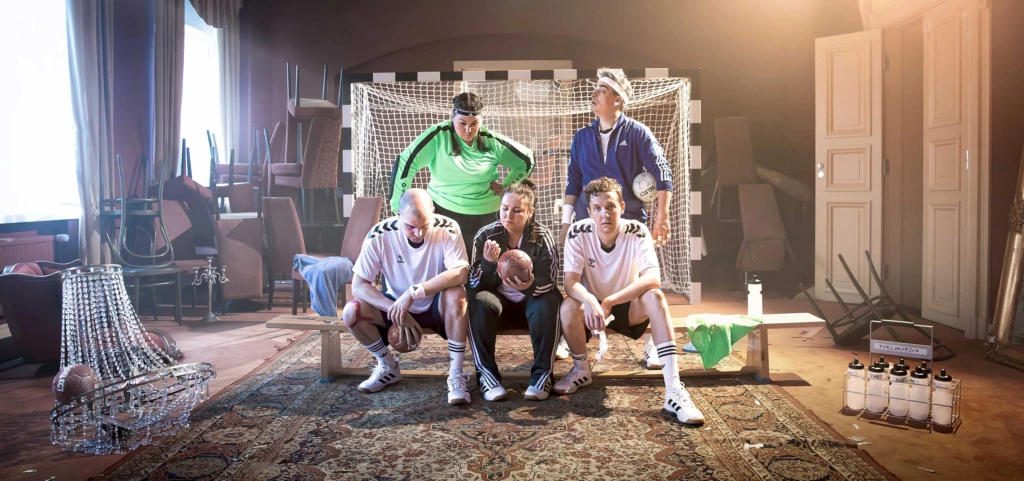 Affischbild för Förlorarna. Fem handbollsspelare är uppställda framför ett handbollsmål. Spelarna ser uppgiva och oengagerade ut.