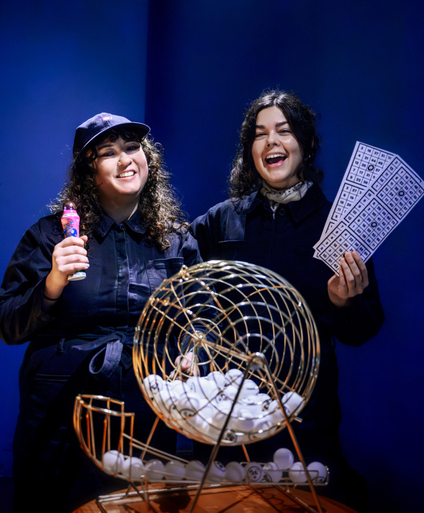 Ett foto två leende kvinnor med bingotillbehör valouva kahdesta hymyilevästä naisesta bingotarvikkeiden kanssa. A photo of two smiling women with bingo accessories.