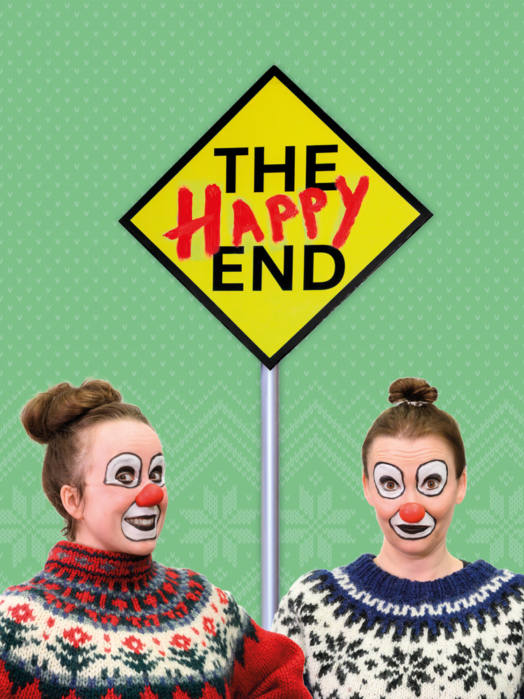 Två clowner i stickade tröjor framför en gul skylt med texten ”The Happy End”. Kaksi klovnia neulepuseroissa keltaisen ”The Happy End” -kyltin edessä. Two clowns in knitted sweaters in front of a yellow sign reading “The Happy End”.